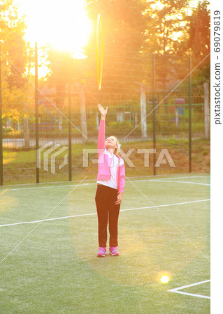 Girl in a tracksuit with a hoop in her hands on the playground 69079819