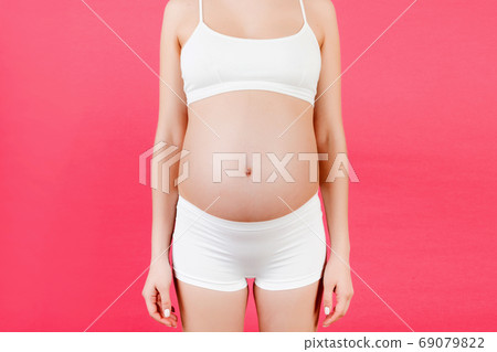 Cropped image of pregnant woman's belly at pink background. Future mom in white underwear. Parenthood concept. Copy space Cropped image of pregnant woman's belly at pink background. Future mom in white underwear. Parenthood concept. Copy space 69079822
