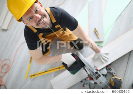 Builder in overalls and hard hat cut laminate on machine in room. 69080495