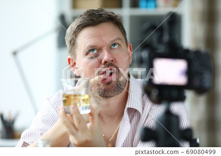 Disheveled man hold glass of alcohol in his hand and taste it with his finger. 69080499