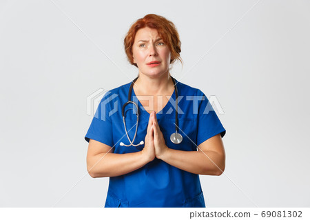 Medicine, healthcare and coronavirus concept. Worried and hopeful redhead female medical worker hoping for end of covid-19 pandemic, praying or pleading with hands clasped together 69081302