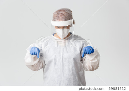 Medical workers, covid-19 pandemic, coronavirus concept. Doubtful and curious female doctor in personal protective equipment ask question about product or treatment, pointing fingers down indecisive Medical workers, covid-19 pandemic, coronavirus concept. Doubtful and curious female doctor in personal protective equipment ask question about product or treatment, pointing fingers down indecisive 69081312