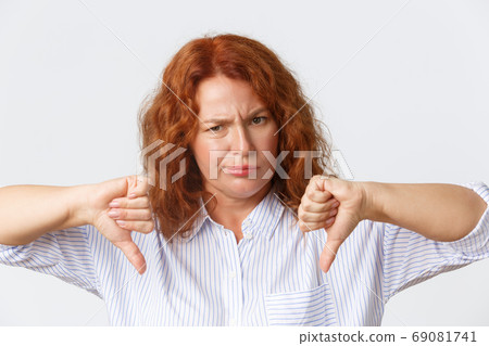 People, emotions and lifestyle concept. Close-up of disappointed and upset, frowning middle-aged redhead woman looking bothered and unamused, showing thumbs-down, dislike and disapproval gesture 69081741