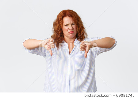 Disgusted middle-aged redhead woman, female entrepreneur grimacing dissatisfied, pointing fingers down and shaking head in rejection, dislike and disapprove something, standing white background 69081743