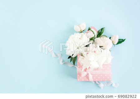 White bouquet of peonies in an envelope for flowers on blue background. Minimal floral concept greeting card. Flat lay, top view. White bouquet of peonies in an envelope for flowers on blue background. Minimal floral concept greeting card. Flat lay, top view. 69082922