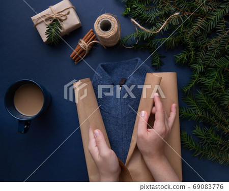 Hands wrapping gift wrapping on blue sweater background Hands wrapping gift wrapping on blue sweater background 69083776