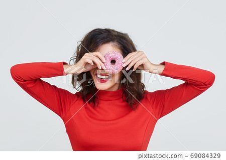 an attractive girl in a red dress looks through a doughnut hole 69084329