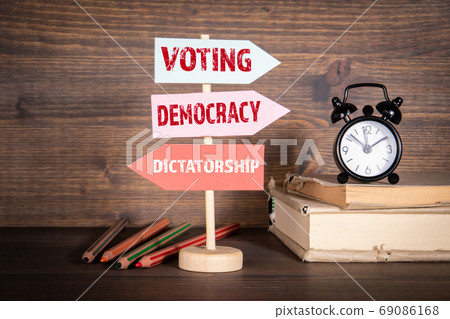VOTING ,DEMOCRACY and DICTATORSHIP concept. Signpost with arrows. Books, alarm clock and pencils 69086168