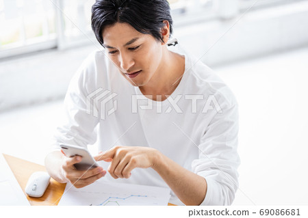 在文書工作期間操作智能手機的年輕人 在文書工作期間操作智能手機的年輕人 69086681