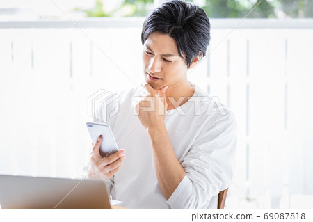 A young man looking at a smartphone during desk work A young man looking at a smartphone during desk work 69087818