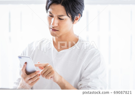 A young man operating a smartphone with a serious look A young man operating a smartphone with a serious look 69087821