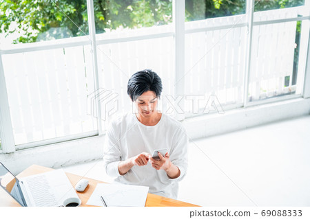 A young man operating a smartphone during desk work A young man operating a smartphone during desk work 69088333