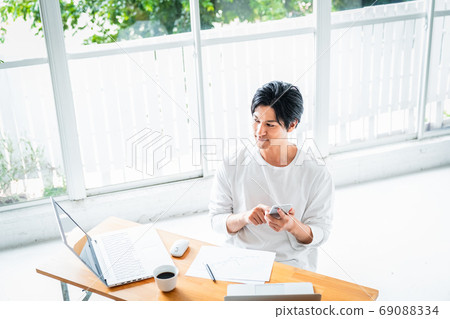 A young man operating a smartphone during desk work A young man operating a smartphone during desk work 69088334