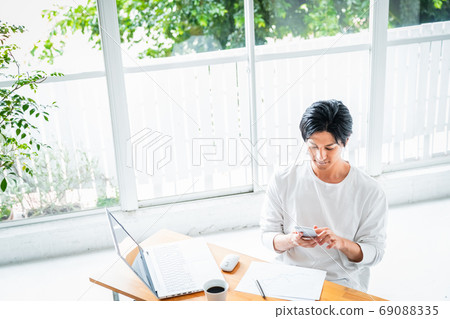 A young man operating a smartphone during desk work A young man operating a smartphone during desk work 69088335