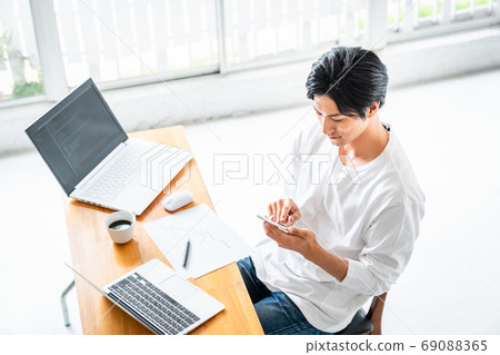 A young man operating a smartphone during desk work 69088365