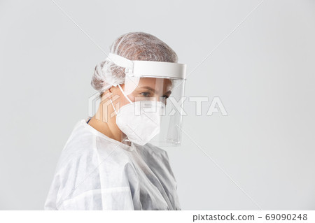 Medical workers, covid-19 pandemic, coronavirus concept. Profile of serious-looking female doctor in personal protective equipment, face shield and respirator listening to patient, provide checkup 69090248