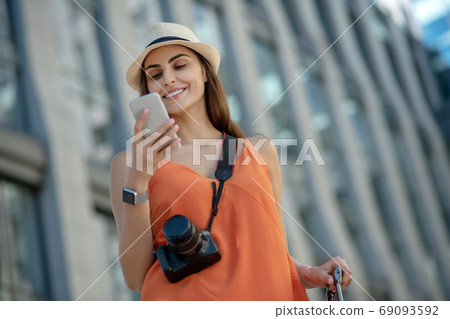 Dark-haired young woman in a hat holding smartphone and reading 69093592