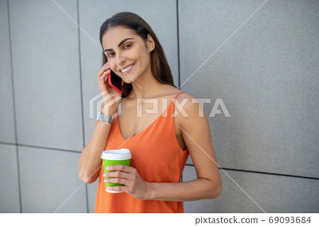 Pretty smiling woman holding a smartphone and a cup of coffee Pretty smiling woman holding a smartphone and a cup of coffee 69093684