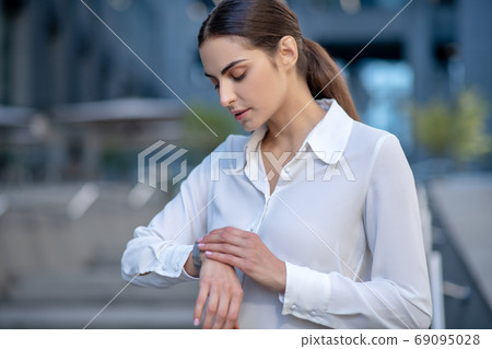 Woman in white shirt looking at smartwatch Woman in white shirt looking at smartwatch 69095028