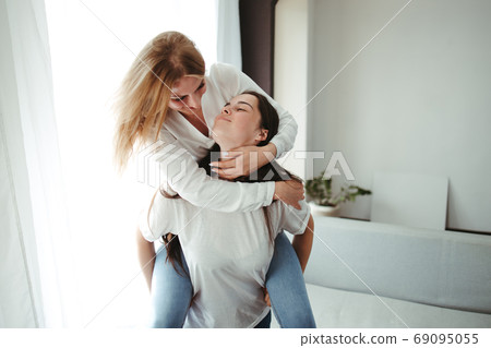 Happy playful girlfriends giving a piggyback hug 69095055
