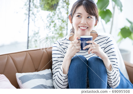 Lifestyle A young woman sitting on a sofa and relaxing with coffee Lifestyle A young woman sitting on a sofa and relaxing with coffee 69095508