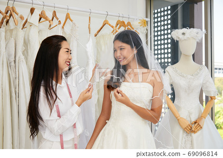 Asian bride trying on wedding dress with female tailor having fun and smiling 69096814
