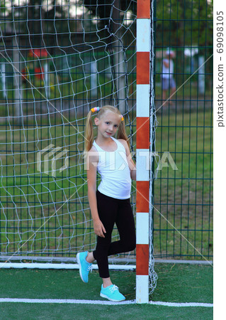 A girl posing near a football goal on a sports field. 69098105