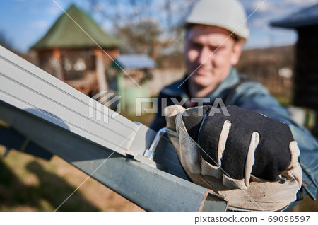 Close-up snapshot of a man's hand wearing a working glove, holding a hex key, installing solar module Close-up snapshot of a man's hand wearing a working glove, holding a hex key, installing solar module 69098597