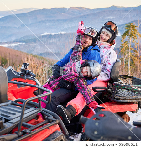 Happy family of three spending great time together in the mountains in winter riding quad bike 69098611