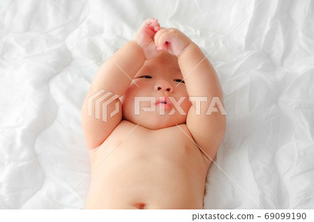 Portrait of a newborn Asian baby on the bed, Charming black-eyed baby 4 month old lies in bed ,A child resting on a bed 69099190