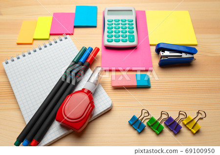 The top view of creative desk with office accessories, notebooks and colorful stickers. Wooden background with copy space for inscription. The top view of creative desk with office accessories, notebooks and colorful stickers. Wooden background with copy space for inscription. 69100950