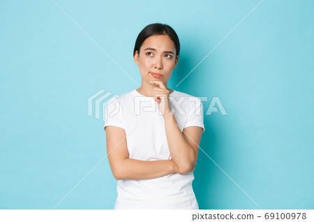 Lifestyle, beauty and shopping concept. Thoughtful and perplexed asian girl thinking, making serious decision, looking upper left corner and pondering, choosing over blue background Lifestyle, beauty and shopping concept. Thoughtful and perplexed asian girl thinking, making serious decision, looking upper left corner and pondering, choosing over blue background 69100978