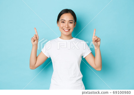 Gorgeous smiling young 20s female asian in casual clothes, pointing fingers up, showing advertisement, demonstrating promo offer. Korean girl indicating at banner, blue background Gorgeous smiling young 20s female asian in casual clothes, pointing fingers up, showing advertisement, demonstrating promo offer. Korean girl indicating at banner, blue background 69100980