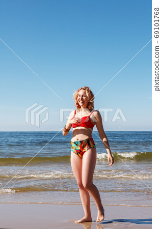 young blonde girl in a red swimsuit standing on the seashore young blonde girl in a red swimsuit standing on the seashore 69101768