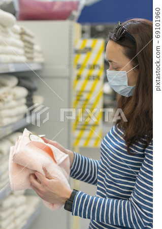 Woman in medical mask choosing goods in a store. Concept of shopping during quarantine at covid-19 pandemic. shopping at the time of the coronavirus. Beautiful young women in a flu mask 69101960