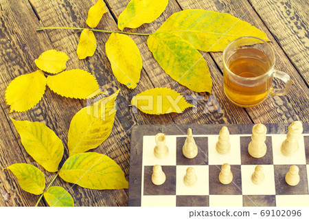 Chess pieces on board, cup of tea and autumn yellow leaves 69102096