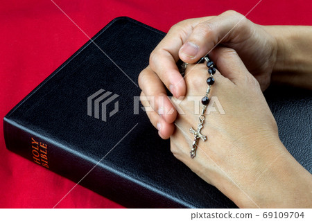 Clasped Hands with Rosary on Closed Bible 69109704