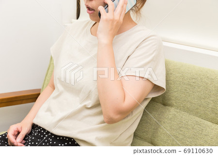 A woman who sits on a sofa and makes a phone call A woman who sits on a sofa and makes a phone call 69110630