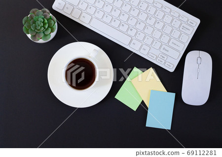 Dark office table with keyboard, plant, cup of coffee and stickers top view Dark office table with keyboard, plant, cup of coffee and stickers top view 69112281