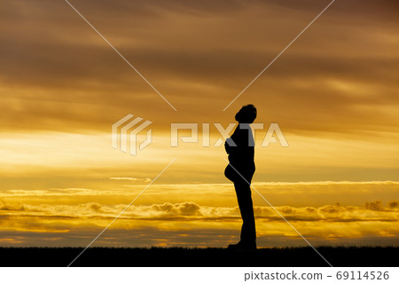 Side view silhouette of a man standing with his arms folded against the setting sun 69114526
