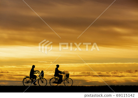 Silhouettes of men and women who go to school by bicycle against the setting sun 69115142