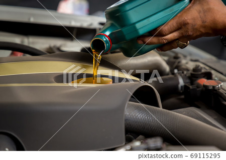 Car mechanic replacing and pouring fresh oil into engine at maintenance repair service station Car mechanic replacing and pouring fresh oil into engine at maintenance repair service station 69115295