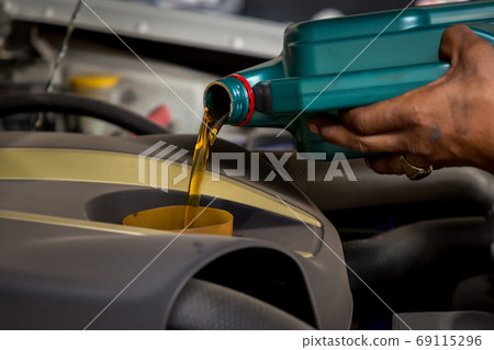 Car mechanic replacing and pouring fresh oil into engine at maintenance repair service station 69115296