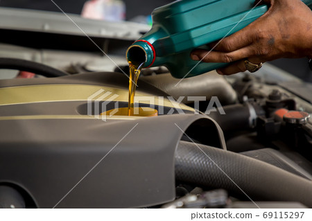 Car mechanic replacing and pouring fresh oil into engine at maintenance repair service station Car mechanic replacing and pouring fresh oil into engine at maintenance repair service station 69115297