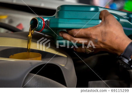Car mechanic replacing and pouring fresh oil into engine at maintenance repair service station Car mechanic replacing and pouring fresh oil into engine at maintenance repair service station 69115299