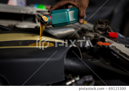 Car mechanic replacing and pouring fresh oil into engine at maintenance repair service station Car mechanic replacing and pouring fresh oil into engine at maintenance repair service station 69115300