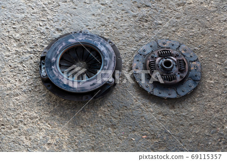 Old Disc Clutch and cover on floor. Old rusty clutch and the disc lies in the garage. Old Disc Clutch and cover on floor. Old rusty clutch and the disc lies in the garage. 69115357