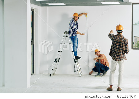 Construction workers measuring wall 69115467