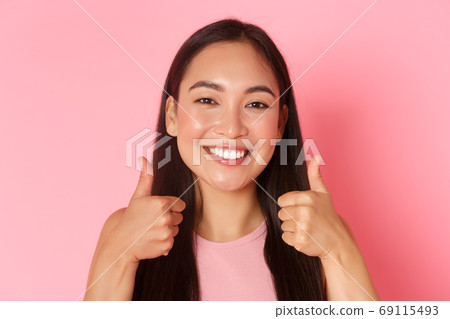 Beauty, fashion and lifestyle concept. Close-up of adorable asian girl looking satisfied, smiling white teeth pleased, showing thumbs-up, compliment good choice, praising or liking something Beauty, fashion and lifestyle concept. Close-up of adorable asian girl looking satisfied, smiling white teeth pleased, showing thumbs-up, compliment good choice, praising or liking something 69115493