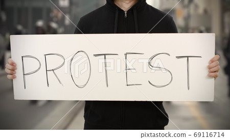 Activist wearing black holds a placard with PROTEST text Activist wearing black holds a placard with PROTEST text 69116714